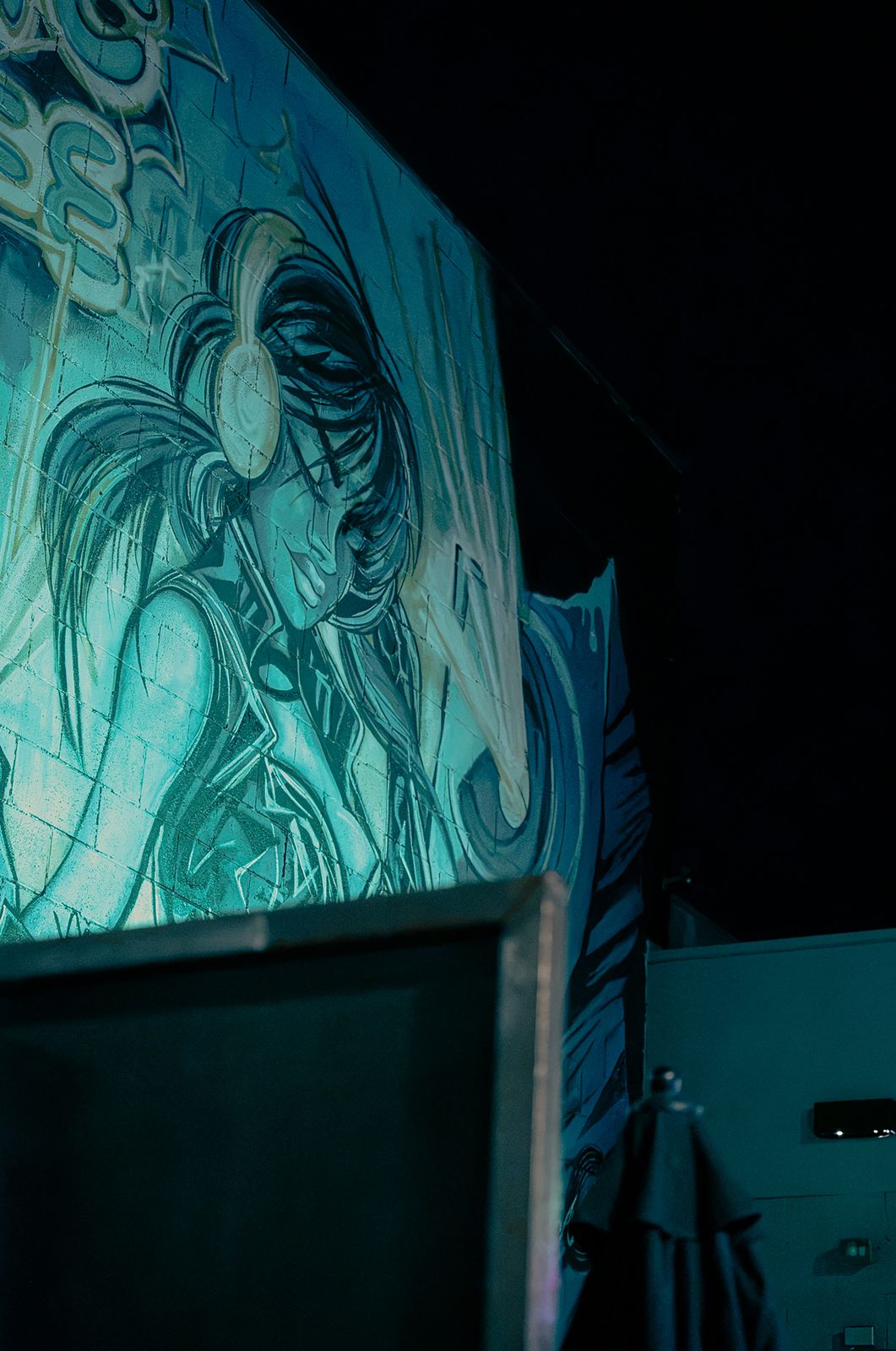 Teal mural lit up on a building wall at night